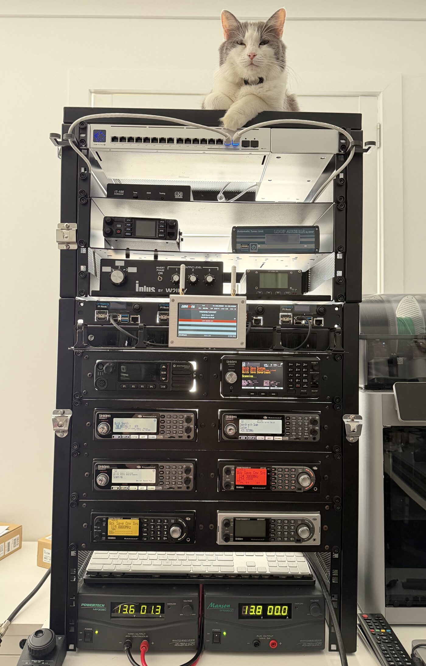 Nathan's home radio rack with multiple amateur radio transceivers, scanners, and digital mode equipment, with his cat sitting on top.